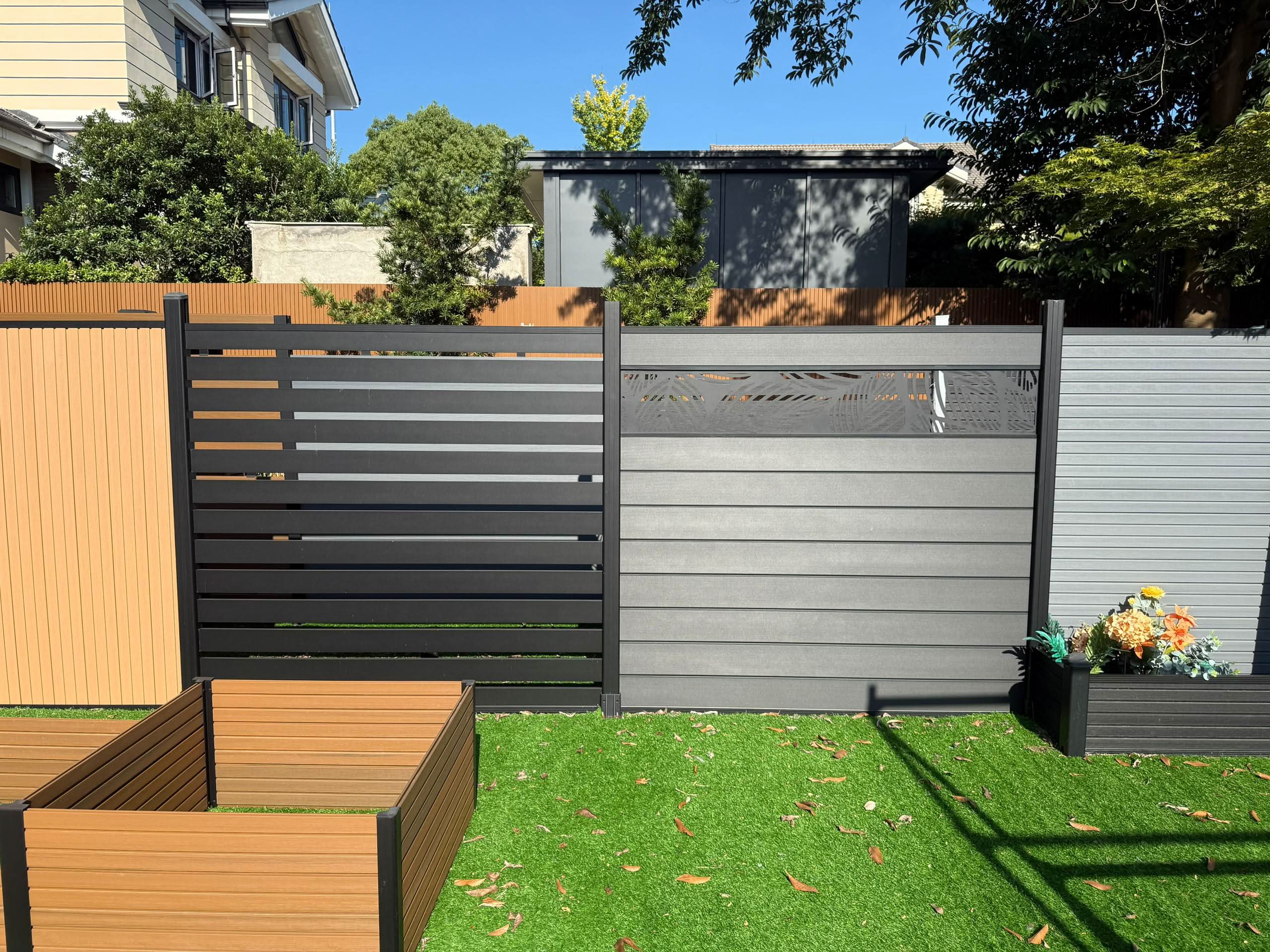 Modern composite fence panels in gray and black with horizontal slats installed in residential backyard