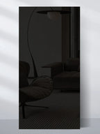 Glossy black wall panel sample reflecting dark modern seating and a curved floor lamp