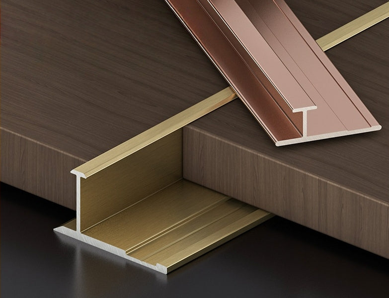 Gold installed H-joint trim with a rose gold aluminum profile displayed above dark wood-look panels