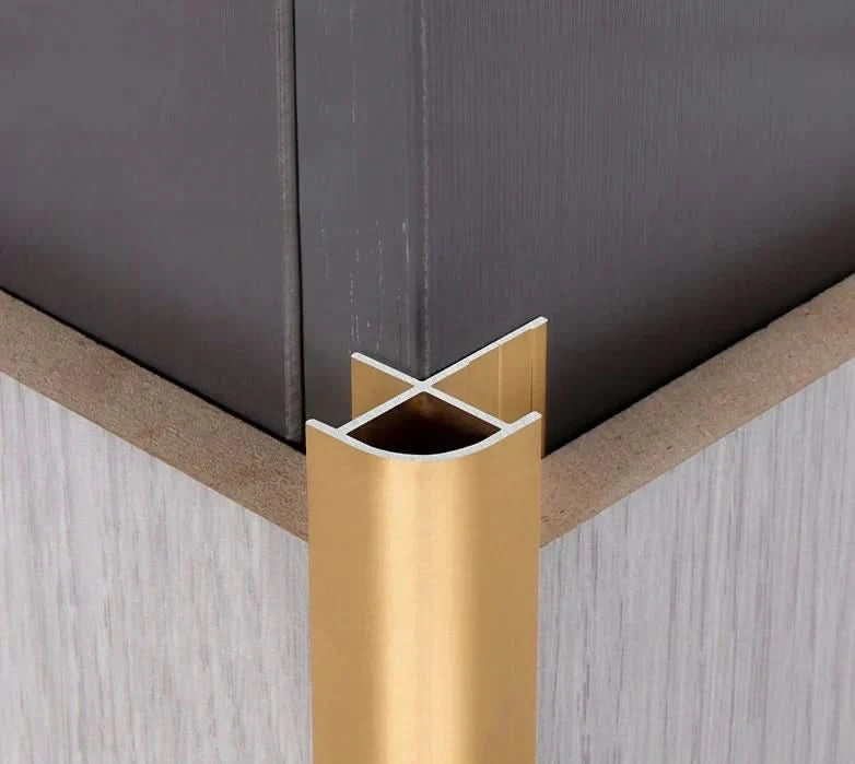 Gold aluminum wall panel outside corner trim installed on interior wall, providing a clean, durable metal edge finish for modern wall panels