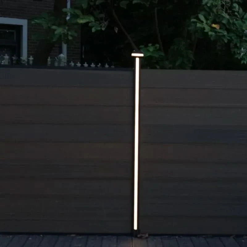 Vertical LED fence post light installed between composite privacy fence panels at night