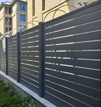 Dark gray composite horizontal slat privacy fence with metal posts installed along residential property