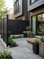 Black aluminum privacy fence installed around a modern paved courtyard with planters