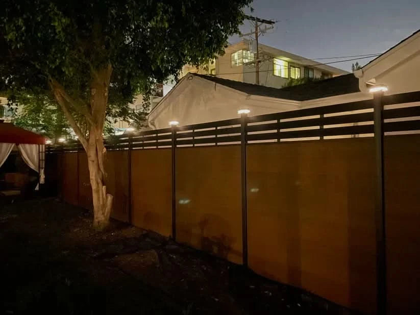Black aluminum privacy fence with horizontal slats and LED post cap lights installed in residential backyard at night