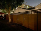 Black aluminum privacy fence with horizontal slats and LED post cap lights installed in residential backyard at night