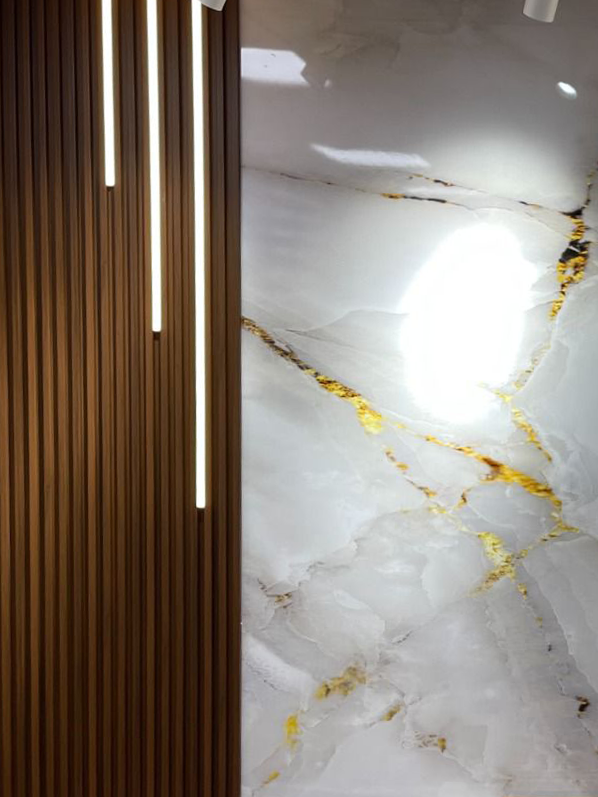 Vertical LED strip accent lighting combined with fluted wood wall panels and marble feature wall