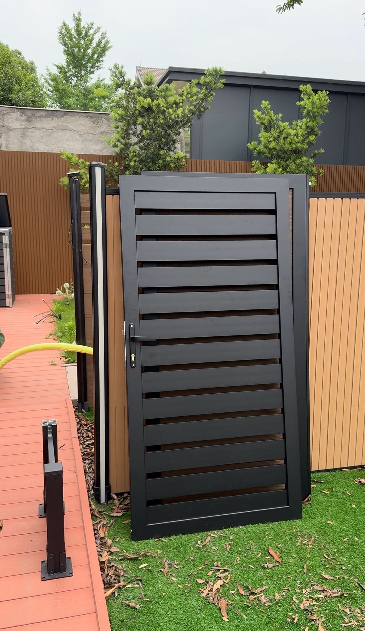 Black composite slatted single fence gate with aluminum frame in modern outdoor setting