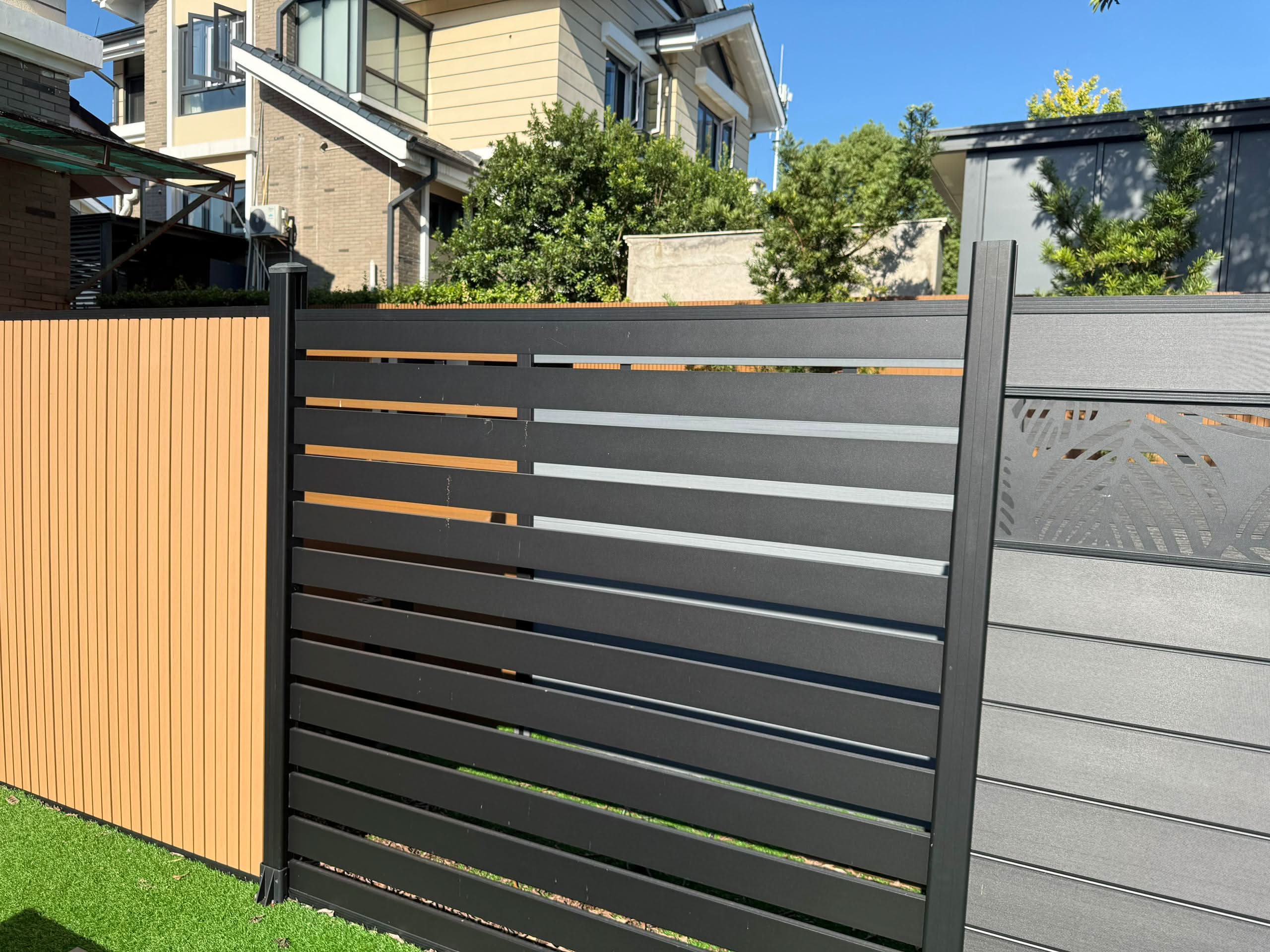 Mixed gray and black composite horizontal slat fence panel installed in residential backyard