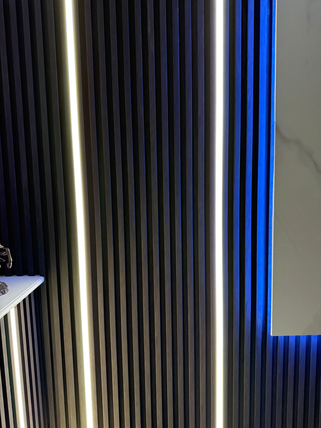 Close-up of recessed vertical LED strip lighting installed within fluted wall panels