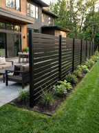 Black aluminum open slat privacy fence beside a home patio and landscaped lawn