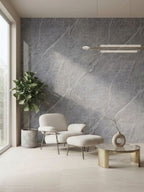 Ash gray marble PVC wall panel behind a cream lounge chair, ottoman, plant, and round coffee table
